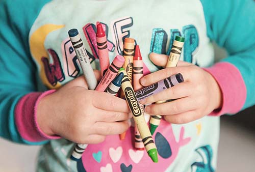 A child holding a bunch of colorful crayons